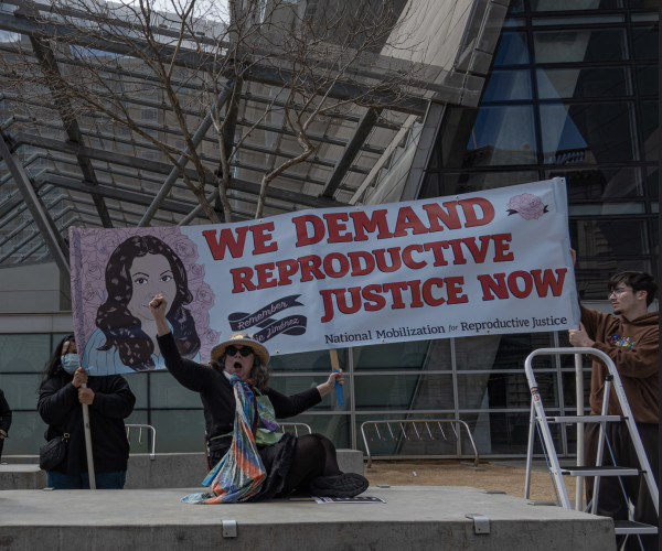 protester raises a fist in front of We Demand Reproductive Justice Now banner